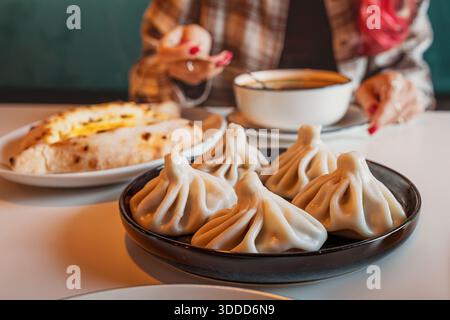 Femme ayant un repas géorgien authentique avec un bol de soupe Kharcho, pain au fromage khachapuri, et boulettes de viande khinkali Banque D'Images