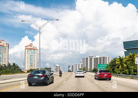 Aventura, États-Unis - 30 avril 2024 : pont routier de la route de Floride dans le comté de Miami Dade avec des palmiers et un panneau bleu ciel pour Country Club Dr. Banque D'Images