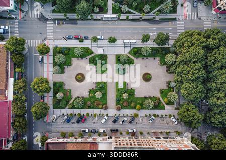 Vue aérienne montrant un parc urbain symétrique avec des espaces verts, des arbres, des allées, des rues environnantes et des voitures garées Banque D'Images