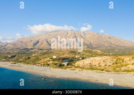 Perspective aérienne panoramique de la plage de Triopetra en Crète, en Grèce, avec une mer turquoise rencontrant une large côte de sable et des montagnes rocheuses spectaculaires s'élevant en arrière-plan sous un ciel bleu clair. Banque D'Images