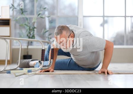 Homme senior allongé sur le tapis après la chute avec marcheur à la maison Banque D'Images