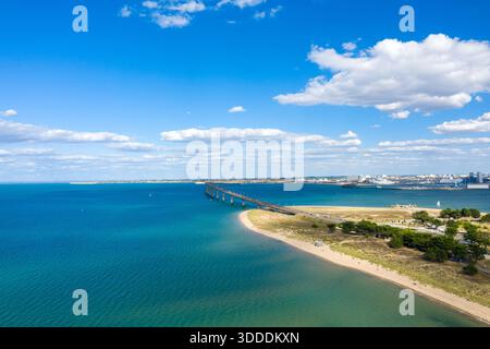 Vue aérienne brillante du Pont de l'Ile de Re qui s'étend à travers l'eau bleu vif de l'Atlantique vers le continent, avec des rivages sablonneux et des nuages de cumulus dispersés au-dessus. L'image capture le paysage marin ouvert et l'atmosphère côtière détendue de la Charente-maritime dans l'ouest de la France. Banque D'Images