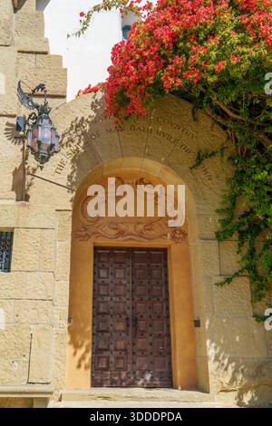 Une entrée de bâtiment en pierre sculptée avec une grande porte voûtée avec des portes en bois cloutées, une lanterne antique et un bougainv rouge coloré Banque D'Images