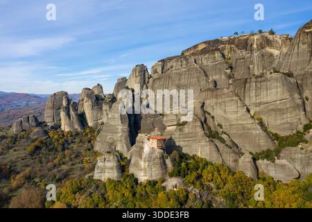 Le monastère d'Agios Nikolaos s'accroche de façon spectaculaire aux falaises abruptes de grès au-dessus d'une forêt colorée d'automne dans les Météores, en Grèce. Les formations rocheuses accidentées et le ciel étendu créent un paysage saisissant et serein. Banque D'Images