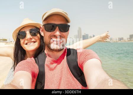 Couple de touristes ayant une vague amusante prendre selfie à la plage de la ville d'Abu dhabi en vacances aux émirats - amis heureux riant ensemble en vacances - les gens Banque D'Images