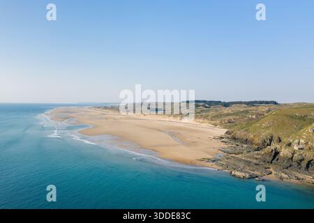 Perspective aérienne d'une vaste plage de sable fin rencontrant des falaises escarpées au Cap de Carteret, avec des vagues turquoises qui chevauchent doucement le rivage sous un ciel bleu clair. Le paysage présente des textures naturelles et une atmosphère sereine et ouverte. Banque D'Images