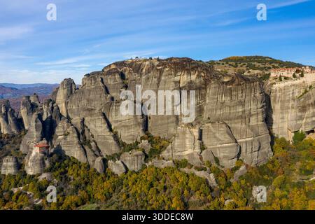 D'anciens monastères se trouvent au sommet d'imposantes falaises de grès entourées d'une forêt d'automne dans les Météores, en Grèce. Le paysage spectaculaire présente des textures rocheuses superposées et des vues panoramiques sous un ciel bleu vif. Banque D'Images