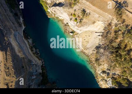 Vue aérienne de haut en bas du canal de Corinthe avec une eau turquoise éclatante, des rives rocheuses abruptes et un terrain aride ensoleillé avec une végétation clairsemée le long du bord. Banque D'Images