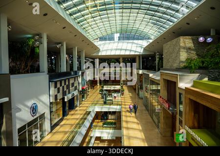 Les gens marchent le long du niveau supérieur du centre commercial Core au toit de verre au centre-ville de Calgary, avec divers panneaux de magasins de détail visibles sur plusieurs fl Banque D'Images