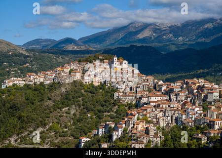 Rivello, en Italie, est perché au sommet d'une colline luxuriante avec des maisons en pierre étroitement groupées et des toits en terre cuite, sur fond de montagnes escarpées sous un ciel bleu avec des nuages éparpillés. Banque D'Images