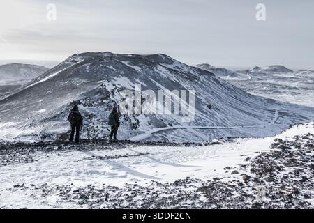 Grindavik, Islande, 2022-02-06 : deux randonneurs se tiennent sur une crête enneigée surplombant un vaste paysage volcanique avec des champs de lave et des montagnes sur la Reykjane Banque D'Images