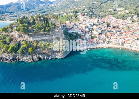 Vue aérienne de la forteresse historique perchée surplombant le village côtier coloré de Parga en Épire, Grèce. La scène présente des falaises escarpées, une végétation luxuriante et des eaux ioniennes turquoises claires sous la lumière du jour. Banque D'Images