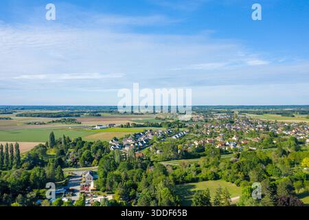 Vue aérienne d'un petit village entouré de champs luxuriants et d'une végétation dense sous un ciel bleu clair. Le paysage présente des terres agricoles ouvertes, des maisons dispersées et un feuillage estival dynamique. Banque D'Images
