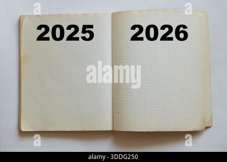 Un cahier ouvert et quadrillé avec les mots 2025 et 2026 écrits sur les pages, symbolisant le changement d'année, la planification, la transition dans le temps et la mendicité Banque D'Images