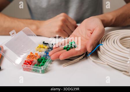 Mains sélectionnant les ferrules de fil de l'organisateur en plastique à côté du câble électrique enroulé sur la table blanche, représentant le bricolage, l'amélioration de la maison et professionnel Banque D'Images