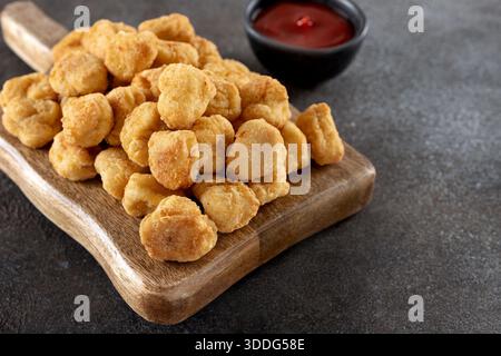 Pop-corn de poulet croustillant sur une planche de service en bois et ketchup sur un fond gris. Gros plan Banque D'Images