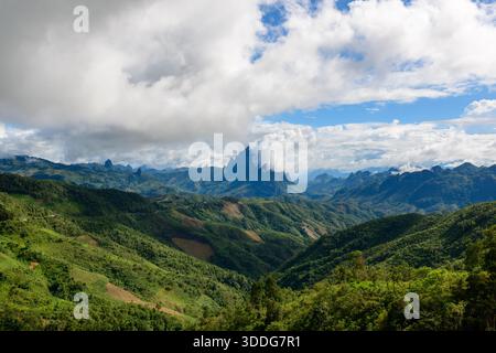 Des collines verdoyantes et des crêtes montagneuses spectaculaires s'étendent au loin sous un ciel rempli d'épais nuages et de taches de bleu. Le paysage présente une végétation luxuriante, des vallées profondes et un sommet accidenté proéminent partiellement enveloppé de brume. Banque D'Images