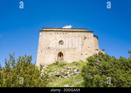 Château en pierre historique se dresse au sommet d'une colline herbeuse à Samitier, en Espagne, sa façade altérée illuminée par la lumière du soleil contre un ciel bleu vibrant et entourée d'arbustes verts. Banque D'Images