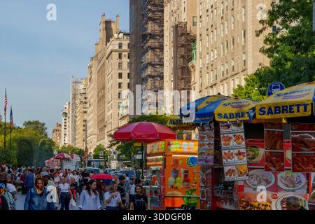 New York, États-Unis. 30 septembre 2025. - Des foules de piétons passent devant des chariots de nourriture vibrants sous des parapluies colorés, avec de hauts bâtiments de la ville bordant un su Banque D'Images