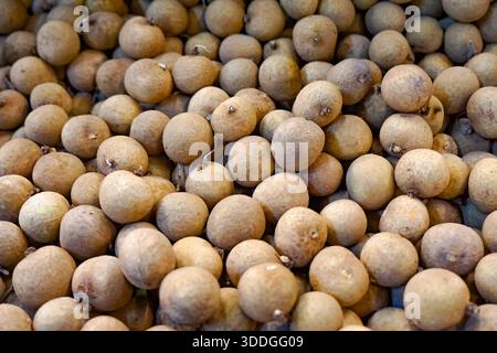 Gros plan de grappes de fruits de longan frais avec une peau brun clair et de fines branches, affichées sur une surface blanche à un étal de marché tropical. Banque D'Images