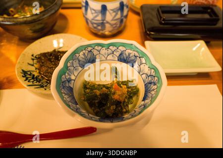 Les haricots verts blanchis enrobés de vinaigrette au sésame sont servis dans un bol en porcelaine bleue et blanche orné. Un éclairage chaleureux met en valeur les textures et les couleurs d'un petit-déjeuner japonais traditionnel. Banque D'Images