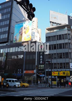 Intersection animée à Jimbocho, Tokyo avec des panneaux lumineux de restaurants, des panneaux d'affichage et des piétons dans un quartier commerçant Banque D'Images