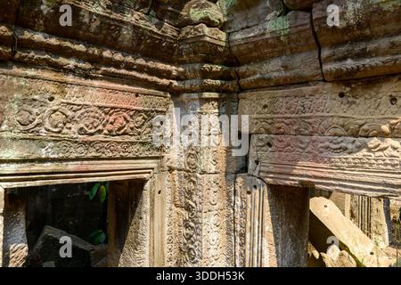 Des sculptures en grès ornées et des linteaux altérés par les intempéries sont illuminés par la lumière du soleil sur un mur extérieur du temple Preah Khan dans la région d'Angkor au Cambodge. Les motifs floraux complexes et les surfaces texturées soulignent le savoir-faire de l'architecture khmère antique. Banque D'Images
