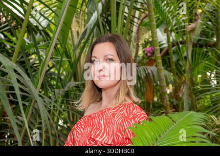 Jolie jeune femme blonde aux cheveux clairs bicolores portant une robe à motif cachemire rouge et blanc, regardant droit dans l'appareil avec un doux sourire Banque D'Images