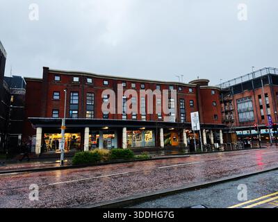 Manchester, Royaume-Uni - 06 décembre 2025 : rue humide à Manchester avec des vitrines en briques rouges et des piétons après la pluie. Banque D'Images