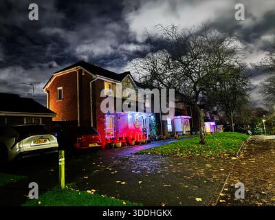 Manchester, Royaume-Uni - 07 décembre 2025 : scène de soirée à Manchester montre une rangée de maisons avec des lumières festives et des voitures garées. Banque D'Images