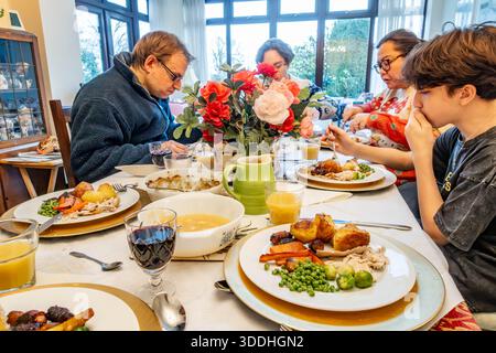 Une famille s'assoit autour d'une table à manger en dégustant un dîner de Noël fait maison Banque D'Images