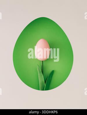 Composition de printemps avec tulipe en œuf de Pâques rose visible à travers un espace en forme d'œuf sur fond vert. Concept de Pâques. Banque D'Images