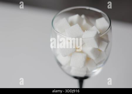 Verre à vin rempli de cubes de sucre blanc sur une table en bois. Concept de sucre caché dans les boissons alcoolisées, le vin sucré et l'information nutritionnelle. Banque D'Images
