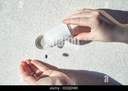 Adulte caucasien versant des gélules vertes du flacon blanc sur la main sous une lumière vive. Banque D'Images