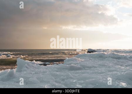 La vague d'hiver se brise près de la glace du rivage dans la lumière chaude du soir. Banque D'Images