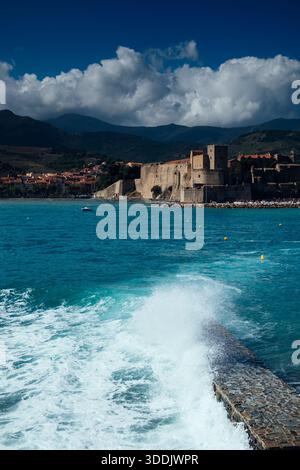 Vagues freinant contre le port de Collioure, plage de Collioure avec le Château Royal de collioure et les montagnes pyranéennes derrière, Côte vermielle Banque D'Images