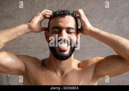 Jeune modèle masculin arabe apprécie la douche du matin, en appliquant shampooing avec joie et soin Banque D'Images