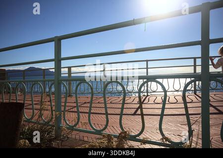 Mer et une falaise par une journée ensoleillée vue à travers la balustrade d'une promenade contreéclairée par le soleil Banque D'Images