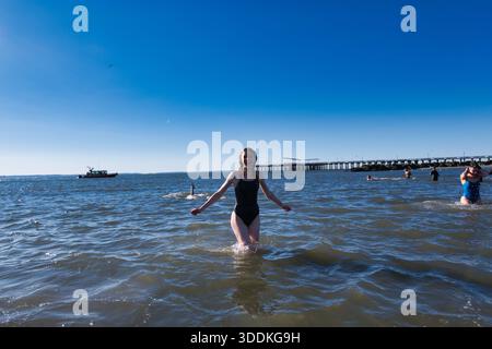 Une jeune femme en maillot de bain noir se tient dans une eau peu profonde, les bras tendus, souriante. Plusieurs autres personnes sont visibles dans l'eau et une tarte Banque D'Images