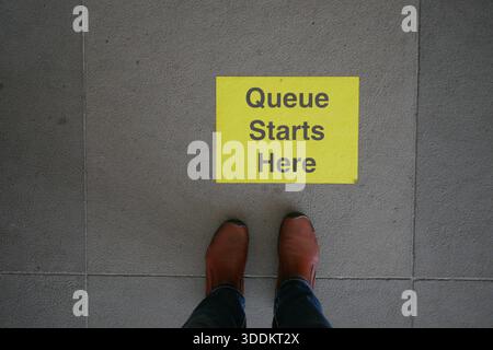 Affiche « la file d'attente commence ici » sur le plancher avec des bottes en dessous Banque D'Images