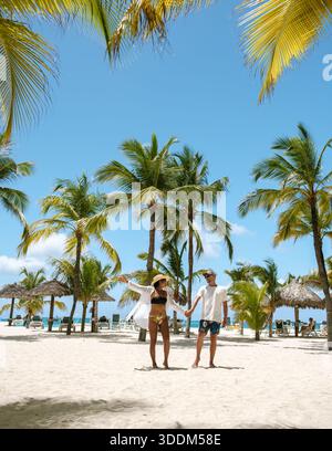 Sous un ciel bleu vif, quelques promenades main dans la main le long des rives sablonneuses de Palm Beach, Aruba. Ils sont entourés par des palmiers oscillants et le Banque D'Images