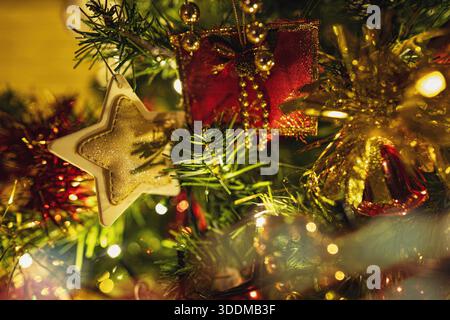 Branches d'arbre de Noël tenant une collection de décorations festives comprenant une étoile dorée étincelante, un ornement rouge en forme de cadeau et une corde chaude Banque D'Images