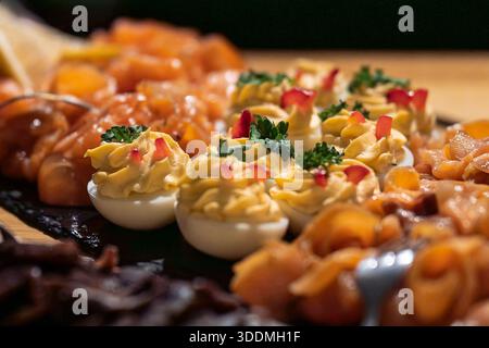 Œufs dévorés garnis d'herbes et de poivrons, servis avec du saumon fumé sur un buffet gastronomique. Gros plan sur les œufs dévorés et les hors-d'œuvre de saumon. Banque D'Images