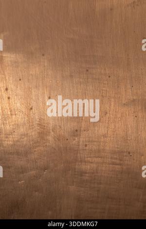 Gros plan d'une feuille de métal brossé aux tons cuivre présentant de petites marques circulaires et de subtiles rayures. La texture chaude et rustique le rend idéal pour le dos Banque D'Images