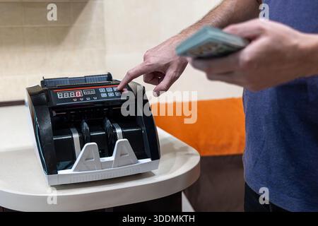 Homme exploitant le comptoir d'argent avec pile d'argent. Personne tenant un paquet de dollars américains tout en appuyant sur des boutons sur une machine de comptage de monnaie électronique Banque D'Images