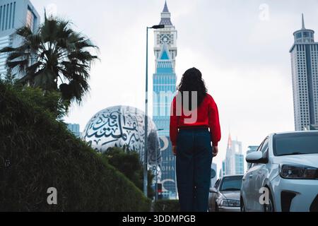 Femme marchant près du Musée du futur avec Sheikh Zayed Road vue sur l'horizon du centre-ville Banque D'Images
