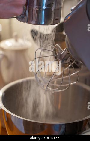 Les mains tamisent la farine dans le bol du mélangeur tout en préparant la pâte charlotte aux pommes sur le comptoir de cuisine en bois, capturant le moment de cuisson à la maison concentré dans une lumière chaude Banque D'Images