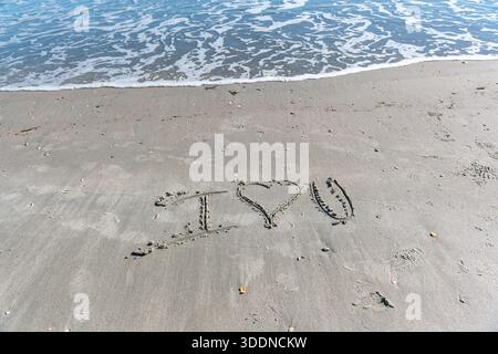 Une plage avec un cœur écrit dans le sable. Le cœur est entouré de rochers et le sable est mouillé. Concept d'amour et de chaleur, comme si quelqu'un avait laissé un M. Banque D'Images