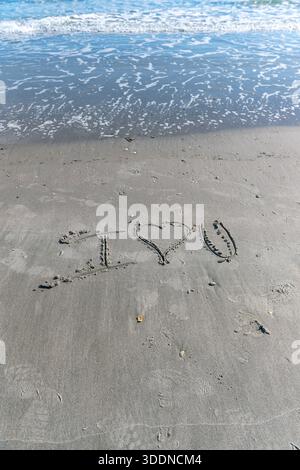 Une plage avec un cœur écrit dans le sable. Le cœur est entouré de rochers et le sable est mouillé. Concept d'amour et de chaleur, comme si quelqu'un avait laissé un M. Banque D'Images