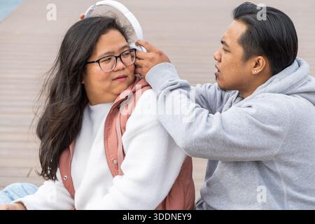 Garçon asiatique d'âge moyen partageant des écouteurs avec sa petite amie Banque D'Images
